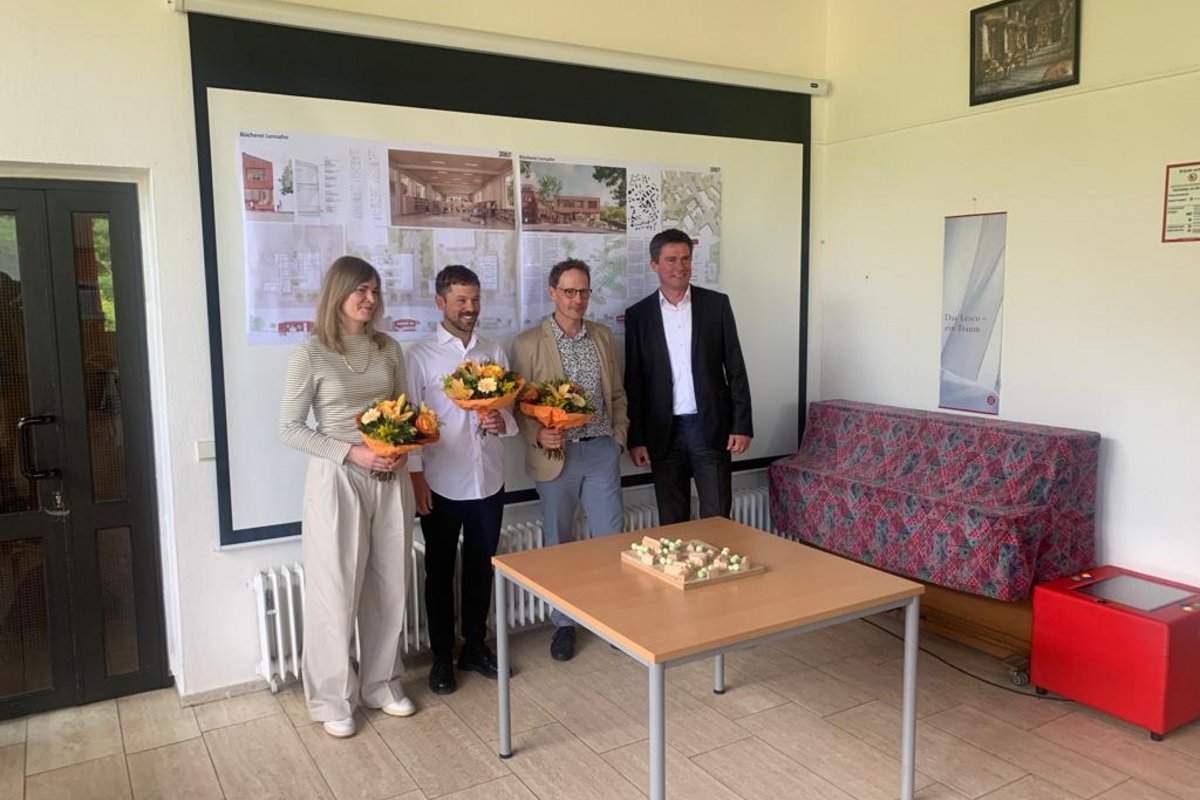 Bürgermeister Michael Robien mit den Gewinnern des Architektenwettbewerbes posieren für ein Foto in der Bücherei