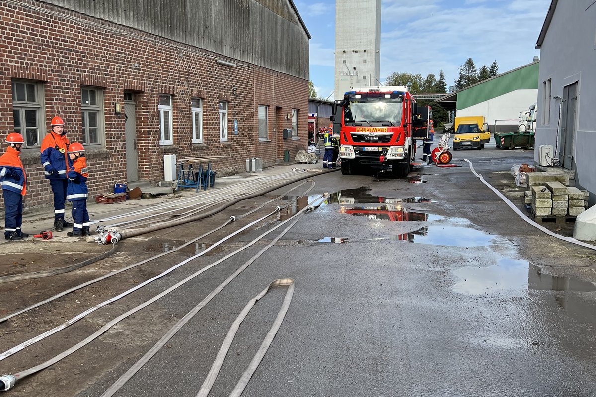 Ausgerollte Löschschläuche auf der Straße, im Hintergrund ein Einsatzfahrzeug der Feuerwehr