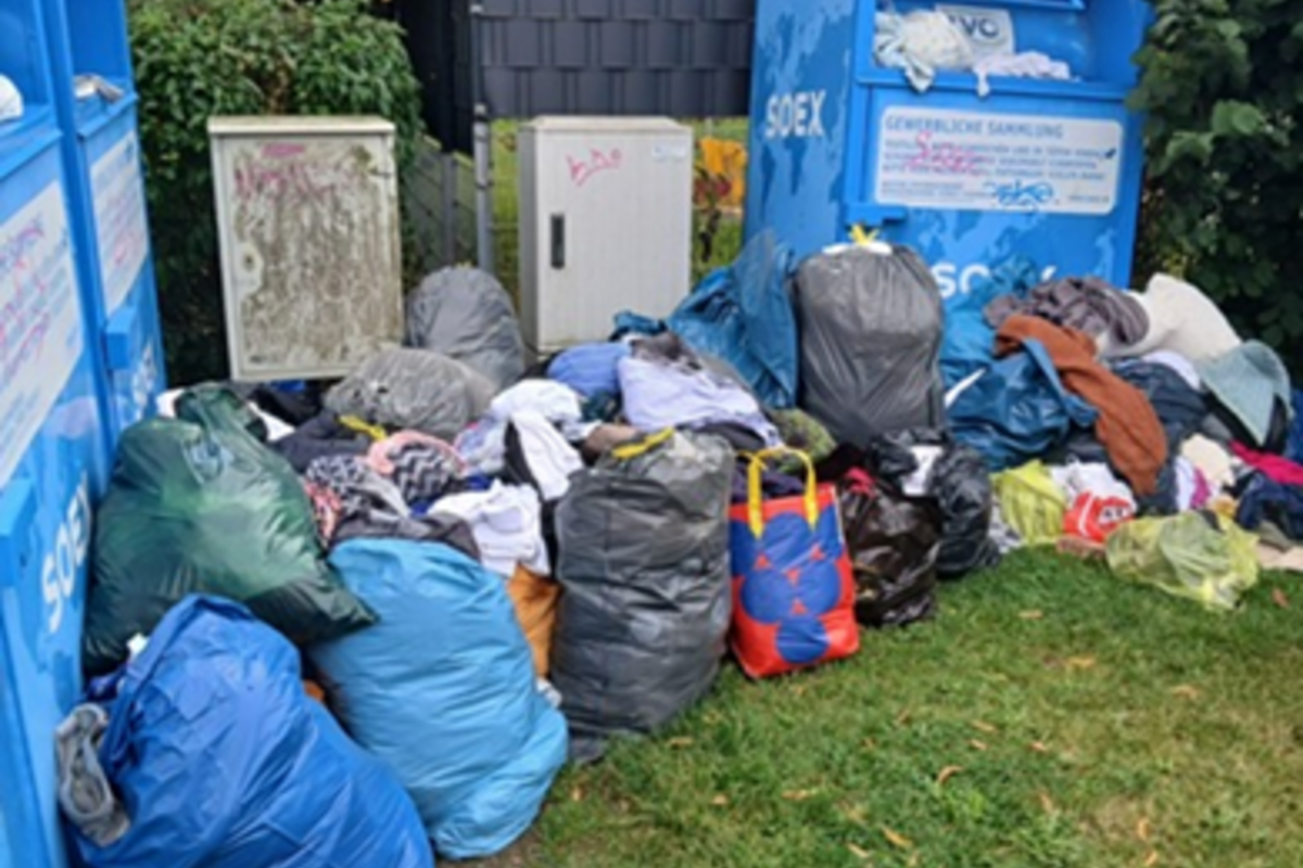 Mehrere blaue und graue Säcke stehen vor den Kleidercontainern