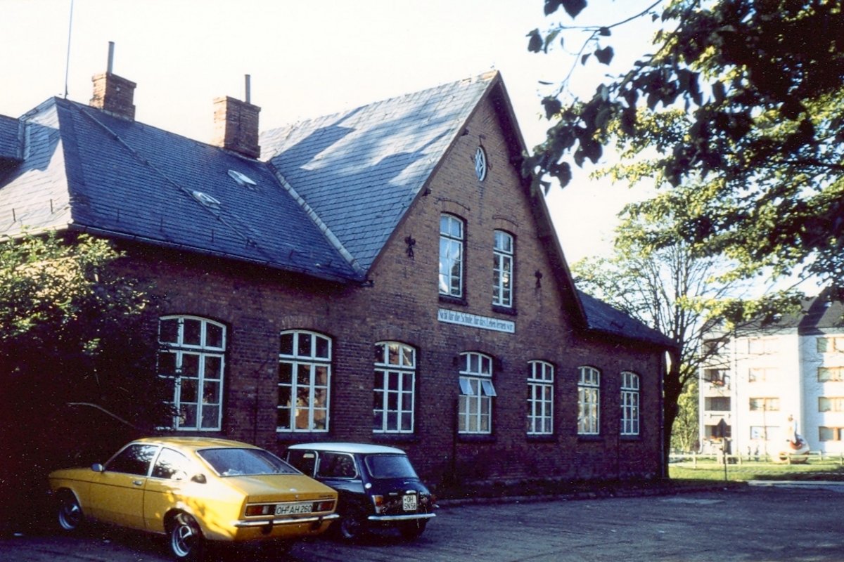 Zwei Fahrzeuge stehen vor dem alten Schulgebäude im Jahre 1977