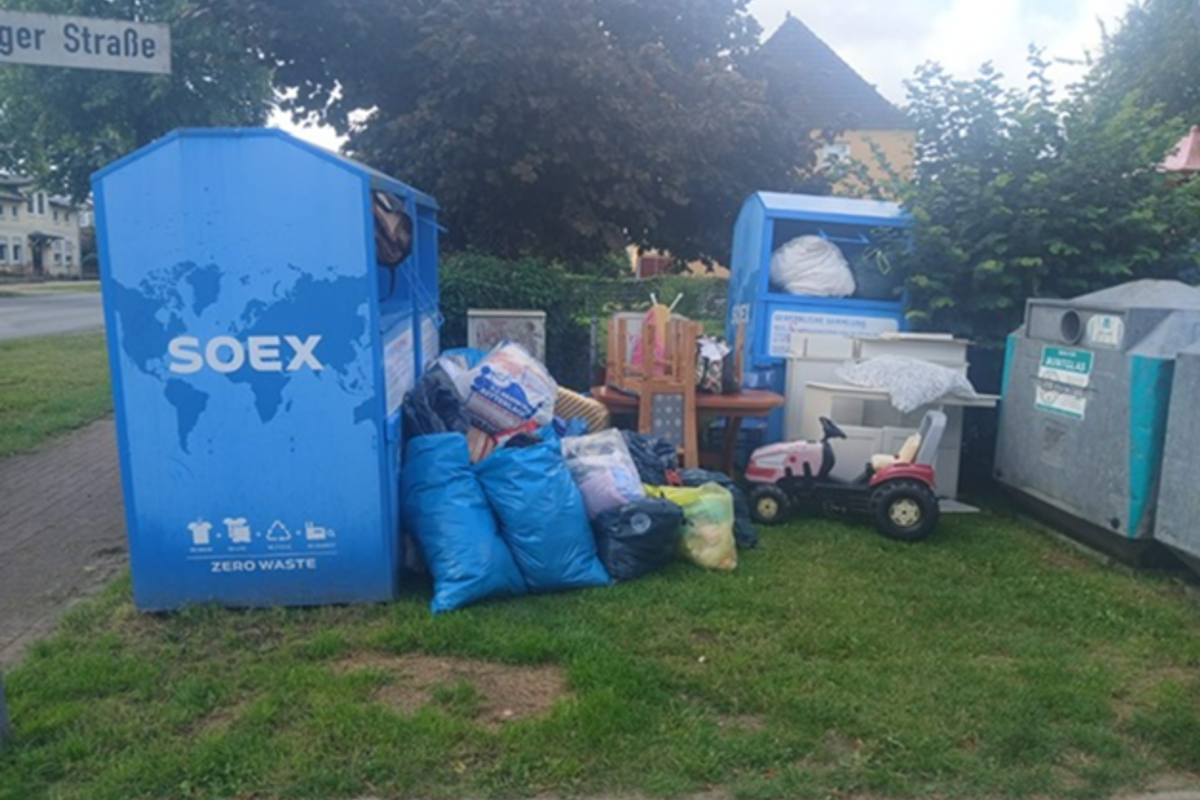 Mehrere blaue und graue Säcke stehen vor den Kleidercontainern