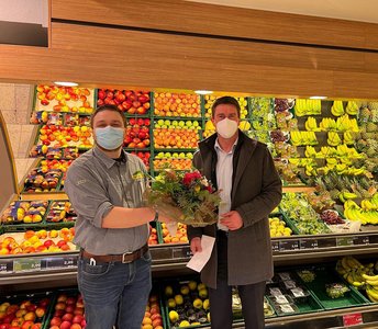 Vor dem Obst und Gemüsestand im Edeka-Markt übergibt der Bürgermeister Michael Robien einen Blumenstrauß an den neuen Filialleiter Herrn Lüders
