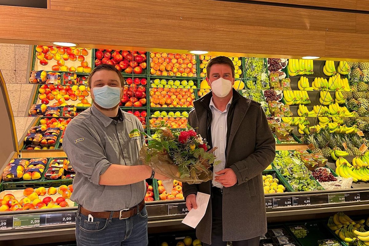 Vor dem Obst und Gemüsestand im Edeka-Markt übergibt der Bürgermeister Michael Robien einen Blumenstrauß an den neuen Filialleiter Herrn Lüders
