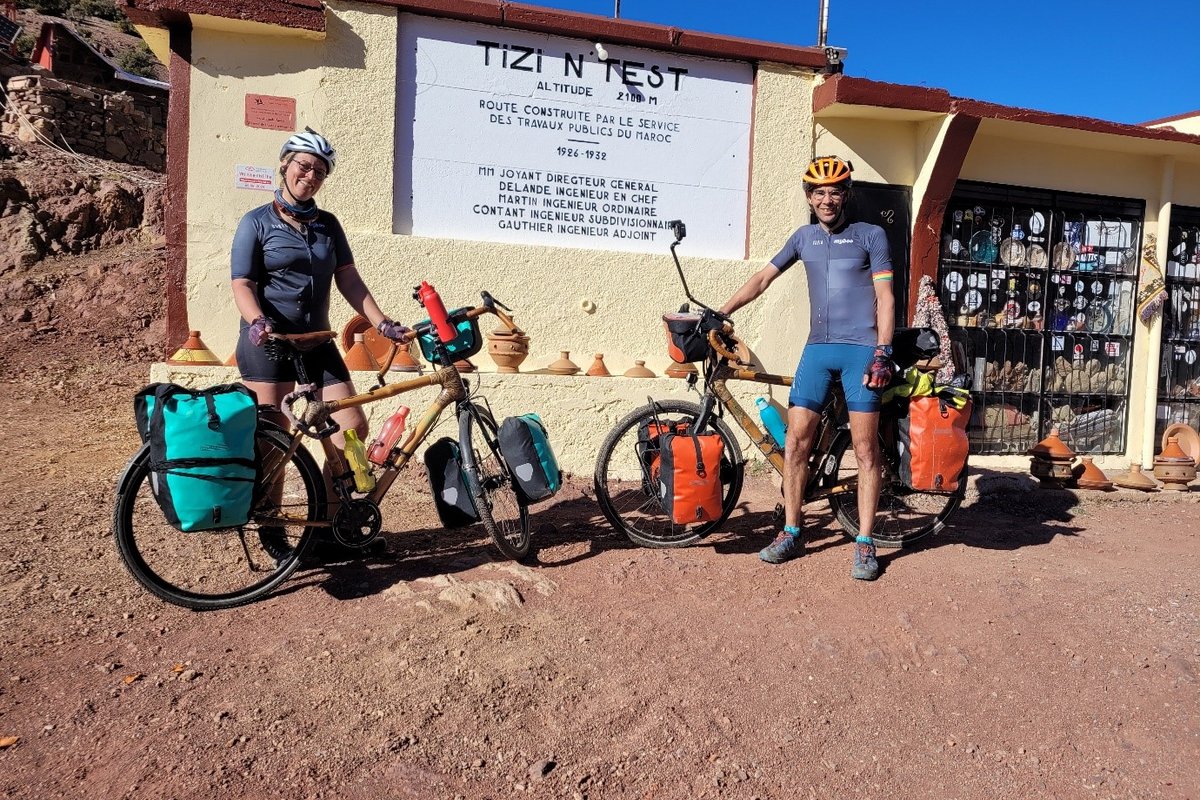 Eheleute Leroyer stehen auf Sandboden vor einem Laden, im Hintergrund ein Berg